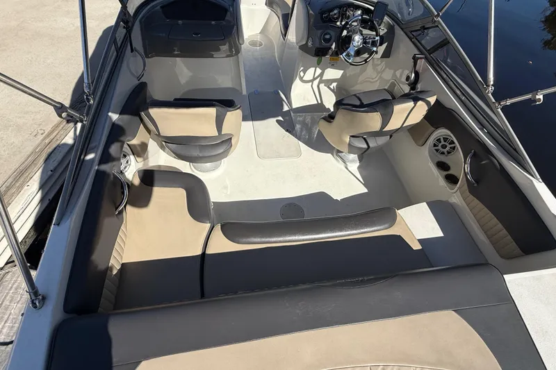 Slide: The Image of 2018 Stingray 204 LR boat interior with beige and black seating, steering wheel, and cup holders. - 10