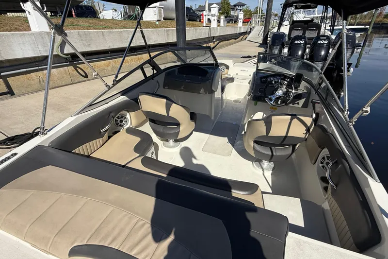 Slide: The Image of 2018 Stingray 204 LR boat interior with beige seating and steering console at a dock. - 11