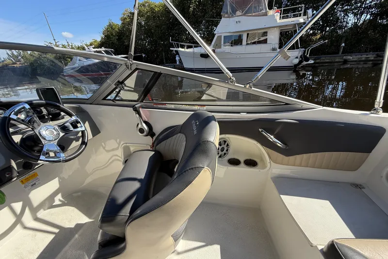 Slide: The Image of 2018 Stingray 204 LR boat interior with steering wheel and seating, docked near other boats. - 14