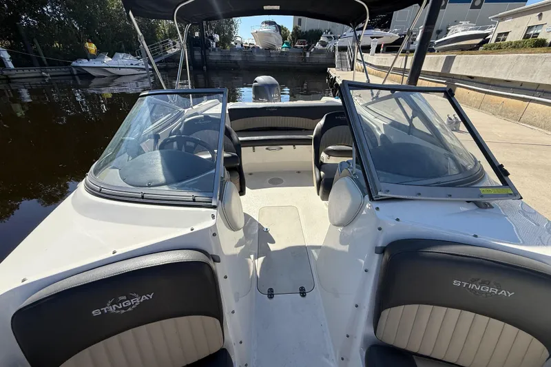 Slide: The Image of 2018 Stingray 204 LR boat interior with dual windshields and seating, docked at marina. - 26