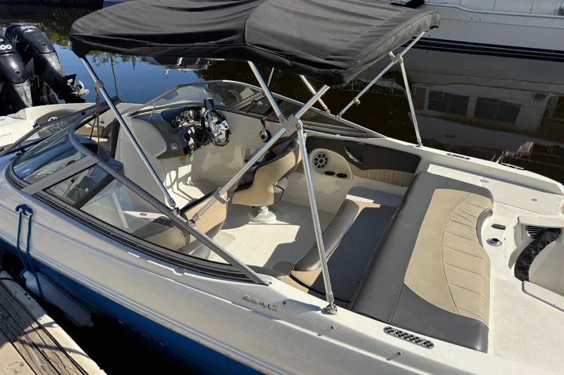 Slide: The Image of 2018 Stingray 204 LR boat with canopy, docked, featuring beige and black interior seating. - 4