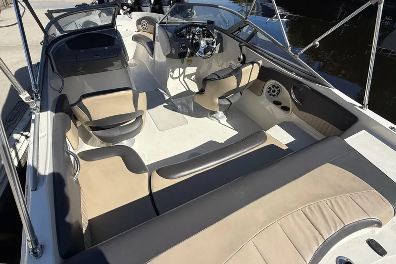 Slide: The Image of 2018 Stingray 204 LR boat interior with beige and black seating, steering console, and cup holders. - 9