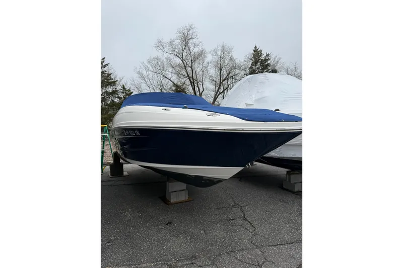 Slide: The Image of 2012 Sea Ray 240 Sundeck boat with blue cover, parked on blocks outdoors. - 14