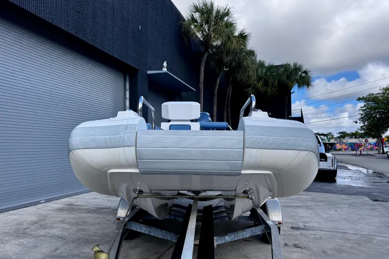 Slide: The Image of 2023 Novurania Catamaran 20 on trailer, parked outside with palm trees and cloudy sky. - 18