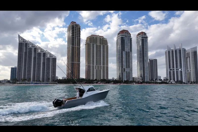 Slide: The Image of Makaira Gen3 26 Outboard 2026 cruising near skyscrapers on water. - 2
