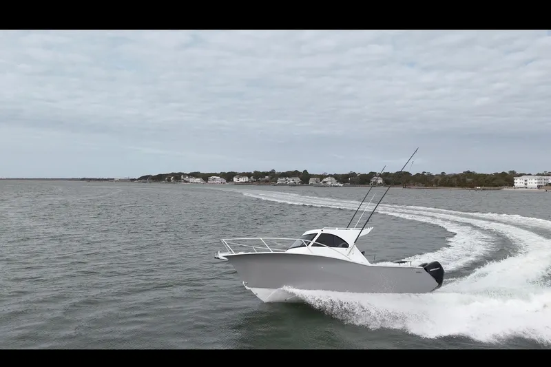 Slide: The Image of 2026 Makaira Gen3 26 Outboard cruising on open water near coastal homes. - 4