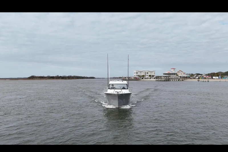 Slide: The Image of Makaira Gen3 26 Outboard 2026 cruising near coastal buildings under cloudy sky. - 7