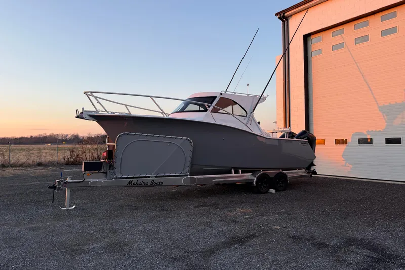 Slide: The Image of 2026 Makaira Gen3 26 Outboard boat on trailer at sunset near a building. - 8