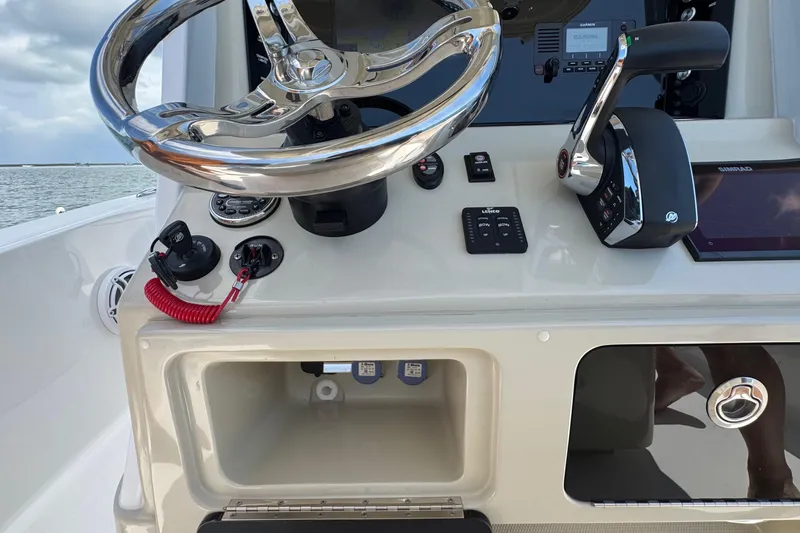 Slide: The Image of 2025 Blackwater 23 Bay boat dashboard with steering wheel and controls, on a calm sea. - 49