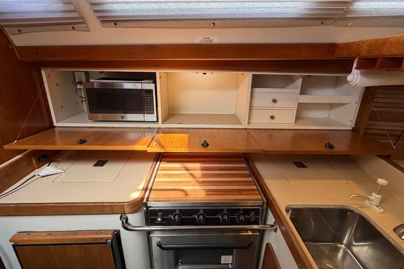 Slide: The Image of 1998 Catalina 380 yacht kitchen with microwave, stove, sink, and wooden cabinetry. - 21