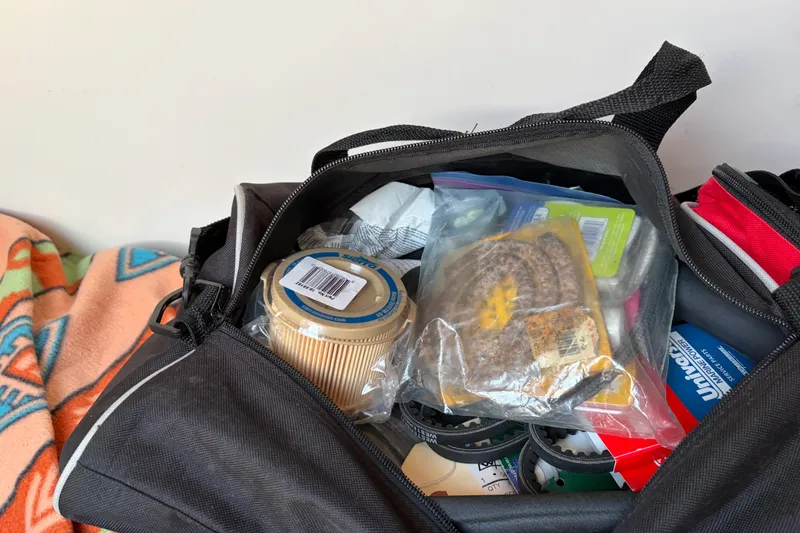 Slide: The Image of Open bag with various items, including filters and packaged goods, on a colorful blanket. Catalina 380, 1998. - 49