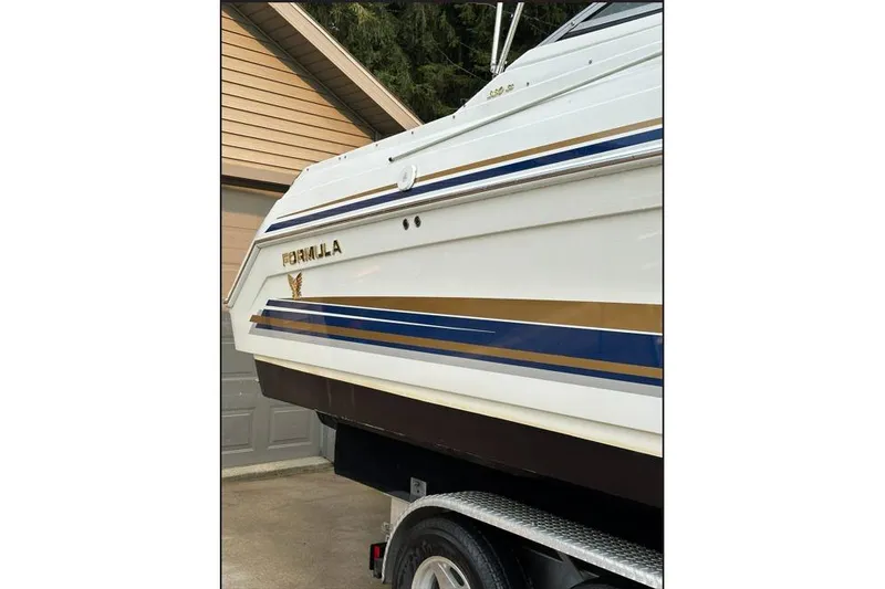 Slide: The Image of 2002 Formula 330 Sun Sport boat with blue and gold stripes on a trailer. - 8