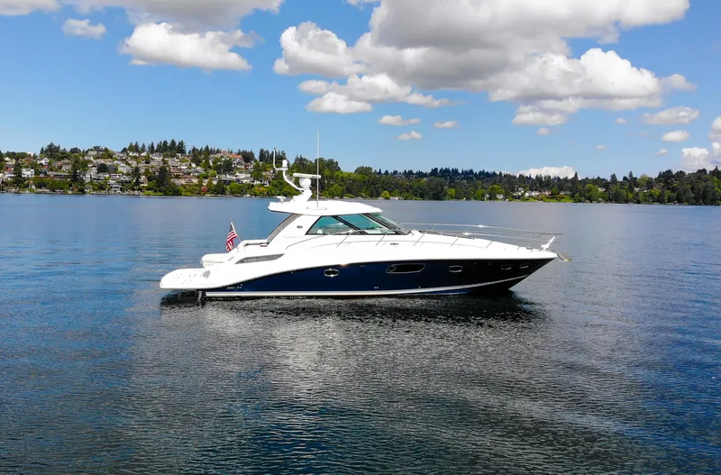 Slide: The Image of 2011 Sea Ray 450 Sundancer yacht on a serene lake under a partly cloudy sky. - 2