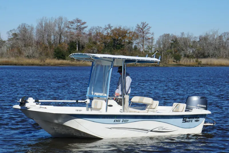 Slide: The Image of 2016 Carolina Skiff 198 DLV boat on calm water, surrounded by trees. - 13