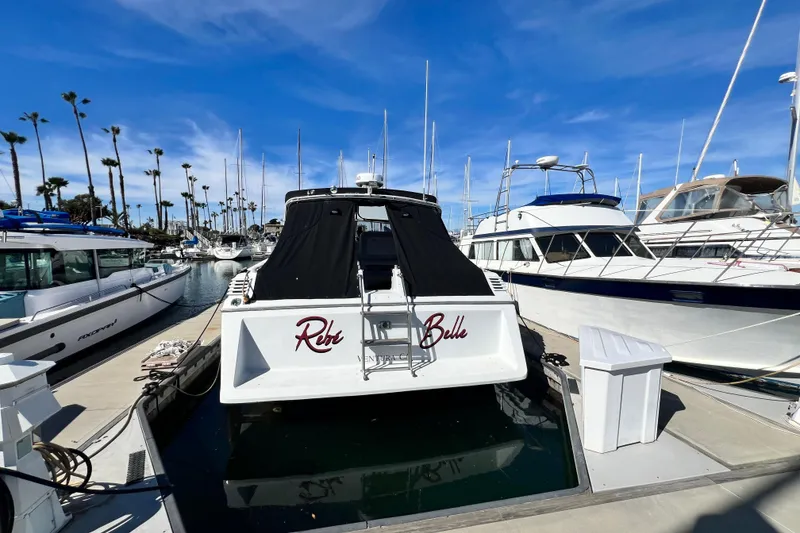 The Image of 1987 Chris-Craft 412 Amerosport yacht docked in a sunny marina with palm trees. - 0