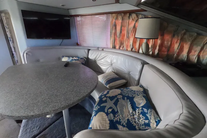 Slide: The Image of 1989 Searay 30 Sedan Bridge interior with curved seating, table, and decorative pillows. - 15