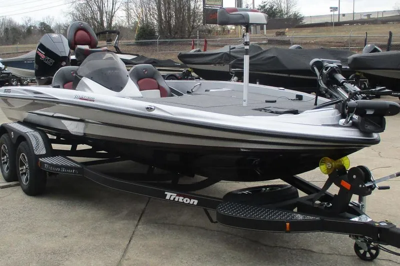 Slide: The Image of 2026 Triton 19 TrX Patriot bass boat on trailer, parked outdoors. - 11