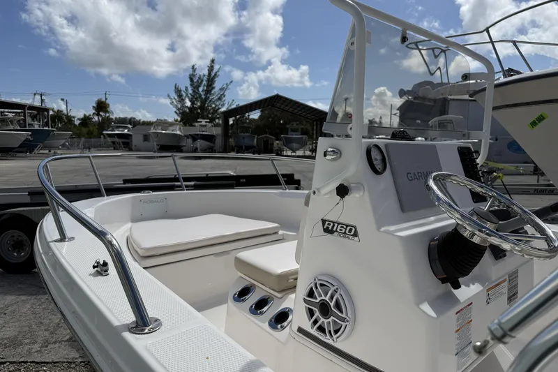 Slide: The Image of 2017 Robalo R160 Center Console boat with steering wheel and seating, docked outdoors. - 5