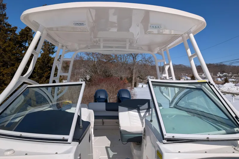 Slide: The Image of 2021 Robalo R247 Dual Console boat with open windshield, white seating, and T-top in snowy landscape. - 13