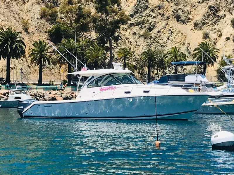 Slide: The Image of 2014 Pursuit OS 385 Offshore boat docked near a rocky shoreline with palm trees. - 2