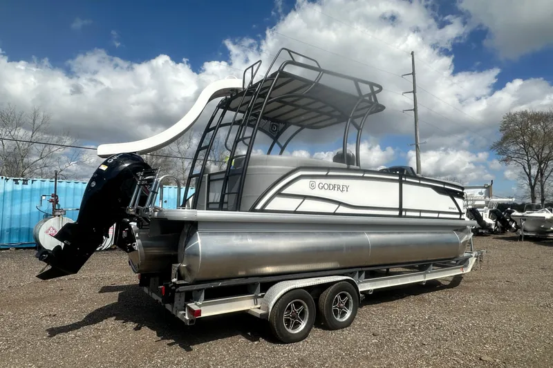 Slide: The Image of 2026 Godfrey Monaco Sun Deck 235 SDC pontoon boat on trailer, under cloudy sky. - 9