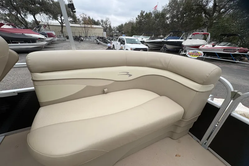 Slide: The Image of 2015 Bennington 20 SLMX boat interior with beige seating in a marina setting. - 10