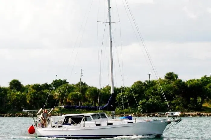The Image of 1966 Vanguard Bermudian Sloop sailing near lush shoreline under cloudy sky. - 0