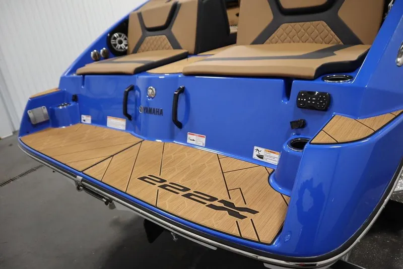 Slide: The Image of 2024 Yamaha Boats 222XE, blue exterior, tan seating, teak-style deck, rear view. - 51