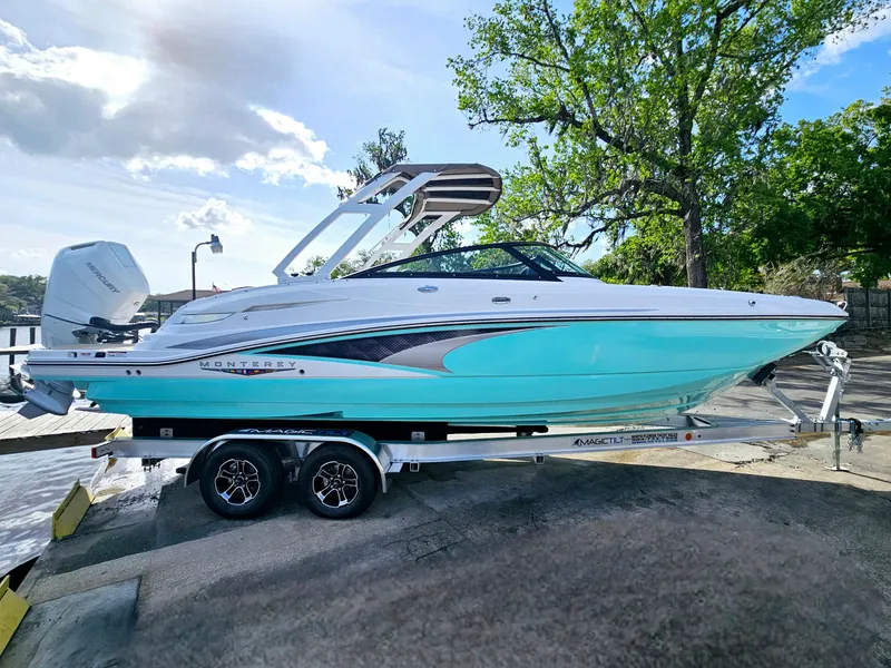 Slide: The Image of 2025 Monterey M-65 boat on trailer, turquoise and white, parked outdoors near trees. - 6