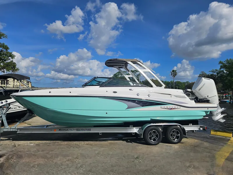 Slide: The Image of 2025 Monterey M-65 boat on trailer, turquoise and white, under a blue sky with clouds. - 2