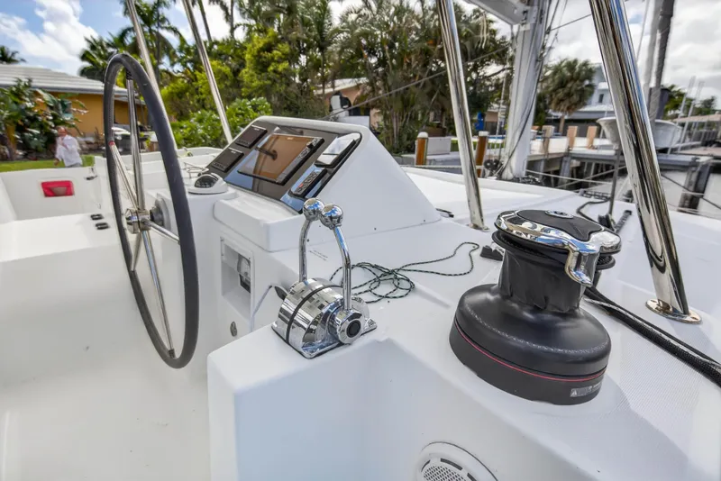 Slide: The Image of Steering wheel and controls of 2019 Lagoon 450 F catamaran, docked with lush surroundings. - 16