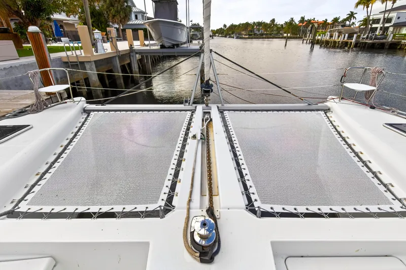 Slide: The Image of 2019 Lagoon 450 F catamaran docked, featuring spacious deck and netting, in a serene waterfront setting. - 27