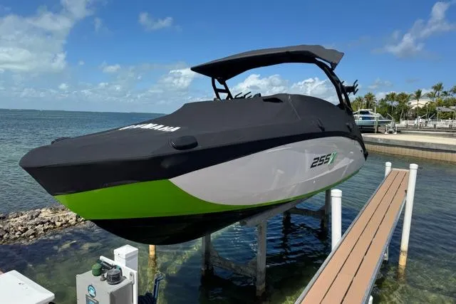 The Image of 2022 Yamaha Boats 255XD on lift by waterfront, featuring sleek design and vibrant green accents. - 0