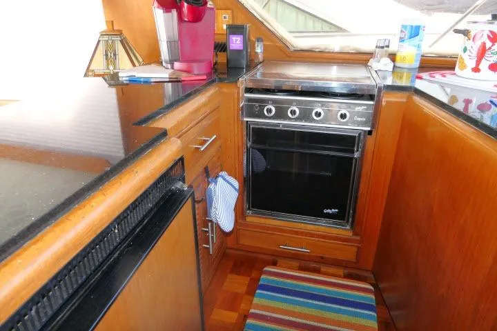 Slide: The Image of 1986 Ocean Alexander 39 Sedan yacht kitchen with stove, wooden cabinetry, and colorful rug. - 16