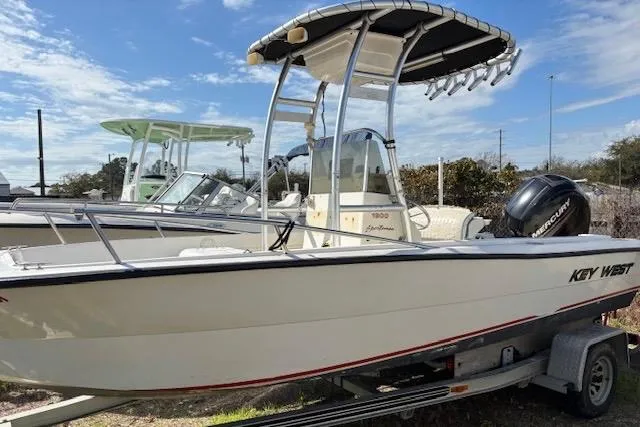 The Image of 1992 Key West 1900 Sportsman boat on trailer, featuring T-top and Mercury outboard motor. - 1