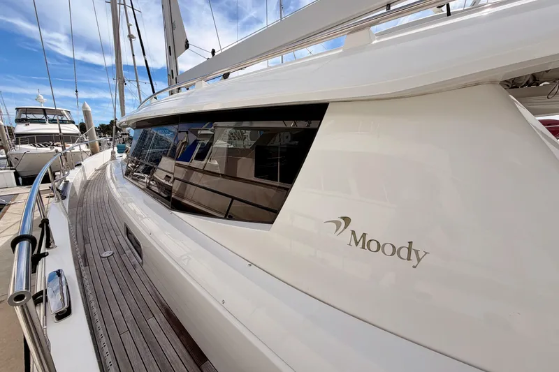 Slide: The Image of 2016 Moody Decksaloon 54 yacht docked, showcasing sleek design and wooden deck. - 16