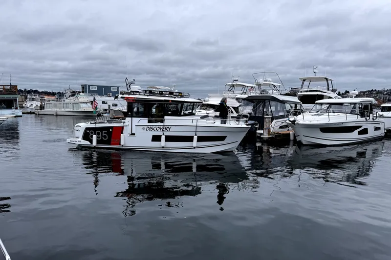 Slide: The Image of 2024 Jeanneau NC 895 Sport boat docked in a marina under cloudy skies. - 26