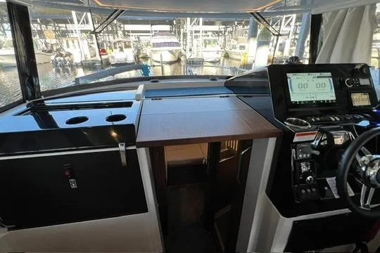 Slide: The Image of 2024 Jeanneau NC 895 Sport interior with seating and table in a marina setting. - 8