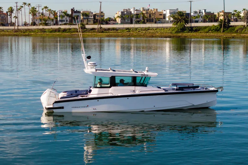 Slide: The Image of 2024 Axopar 29 XC Cross Cabin boat on calm water, with urban backdrop. - 2