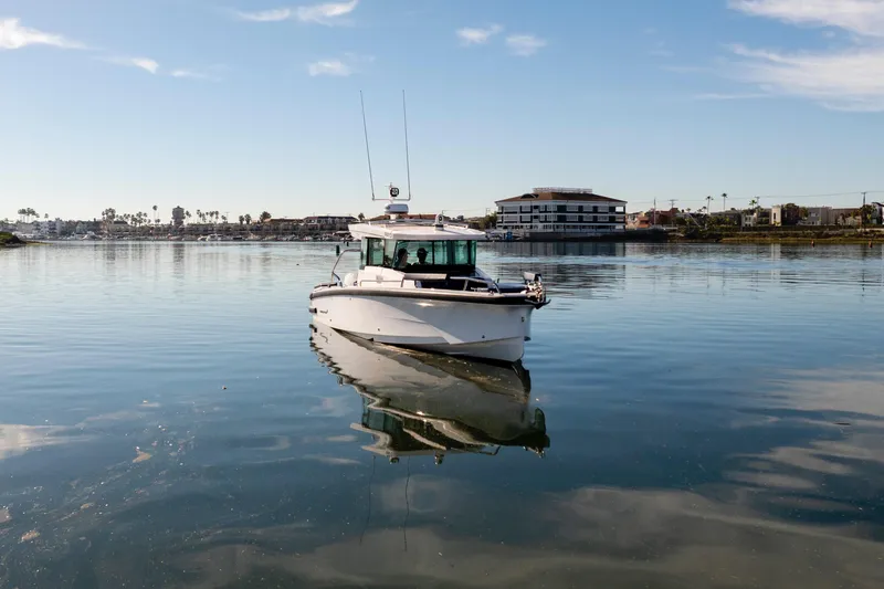Slide: The Image of 2024 Axopar 29 XC Cross Cabin boat on calm water with coastal buildings in the background. - 7