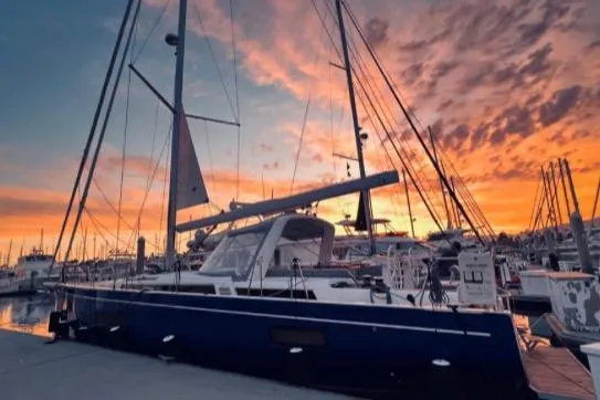 Slide: The Image of 2022 Beneteau Oceanis Yacht 54 docked at sunset, showcasing elegant design and vibrant sky. - 2