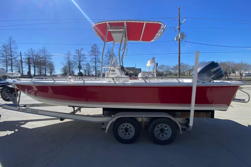 Slide: The Image of 2005 Sea Pro SV2400CC Bay Boat with red hull on trailer, under clear blue sky. - 6