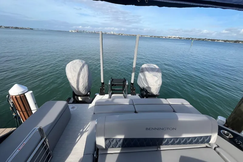 Slide: The Image of 2025 Bennington 30 QX Swingback pontoon boat on calm water, featuring covered engines. - 6