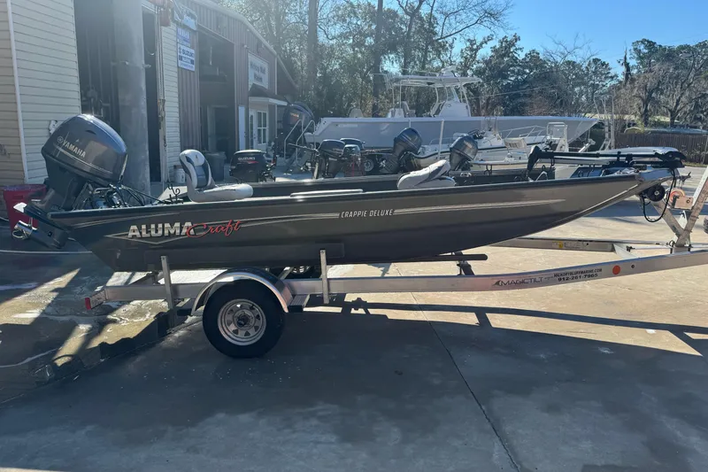 Slide: The Image of 2018 Alumacraft Crappie Deluxe boat on trailer, parked outdoors with Yamaha motor. - 4
