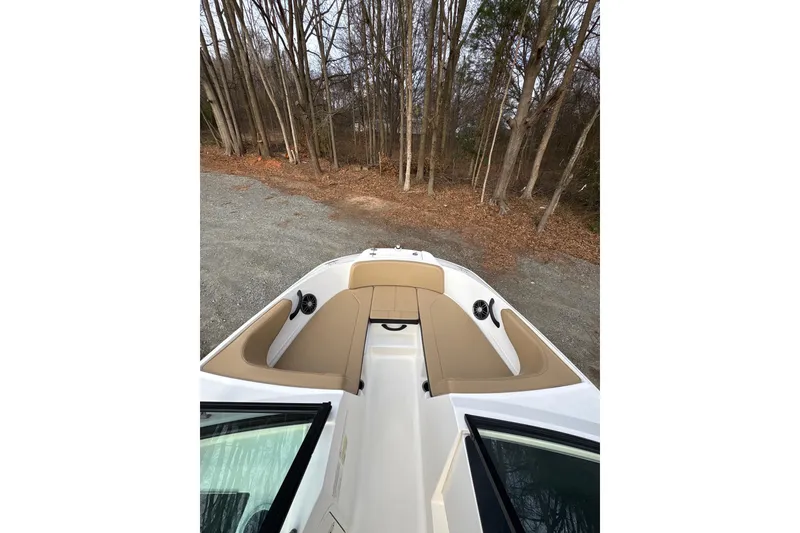 Slide: The Image of 2023 Sea Ray SPX 210 boat interior with tan seating, parked near trees. - 13
