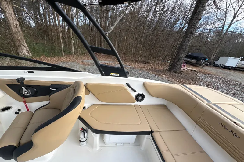 Slide: The Image of 2023 Sea Ray SPX 210 boat interior with tan seating and black accents, parked near wooded area. - 23