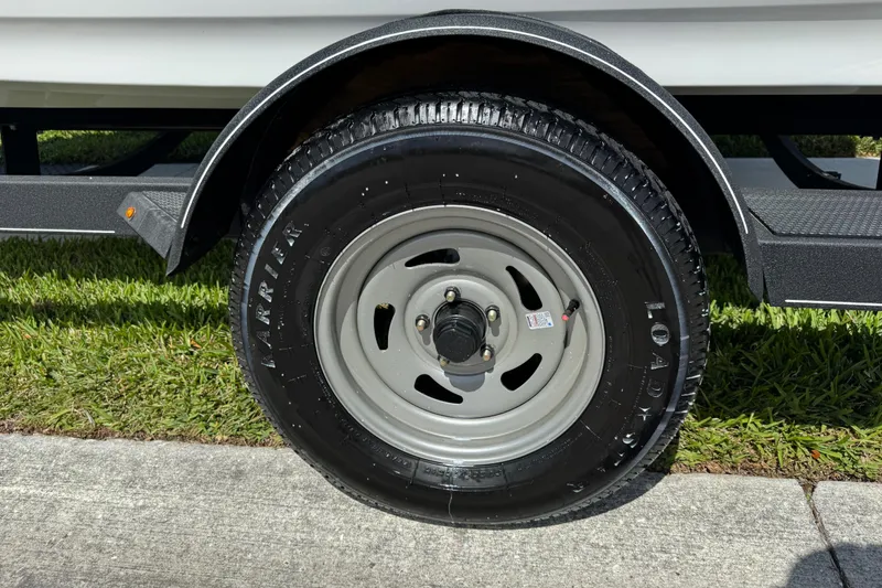 Slide: The Image of 2024 Tahoe 185 S trailer wheel on grass, featuring a black tire and gray rim. - 24