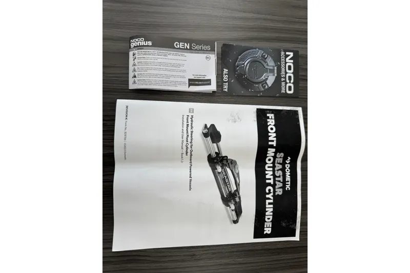 Slide: The Image of NOCO Genius GEN Series and Dometic SeaStar front mount cylinder manuals on a wooden surface. - 93