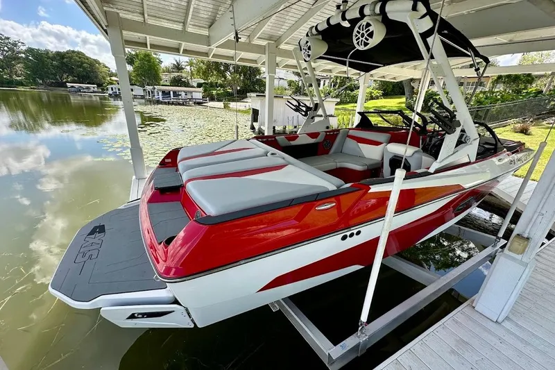 Slide: The Image of 2021 Axis A20 boat in red and white, docked under a covered structure by a lake. - 4