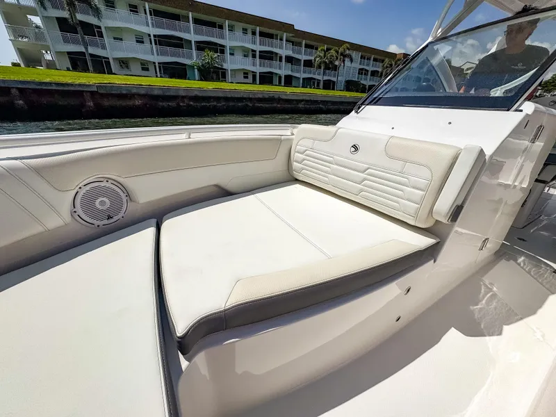Slide: The Image of 2025 Edgewater 262 CX boat interior with white seating and speaker, near waterfront buildings. - 17